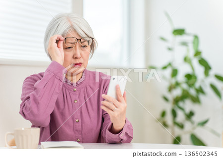 Senior woman who has difficulty seeing the text on her smartphone due to presbyopia (smartphone presbyopia, reading glasses, focus, eye strain) Senior woman who has difficulty seeing the text on her smartphone due to presbyopia (smartphone presbyopia, reading glasses, focus, eye strain) 136502345