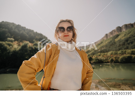 Woman in Yellow Raincoat Posing in Front of Mountains and Lake Woman in Yellow Raincoat Posing in Front of Mountains and Lake 136503395