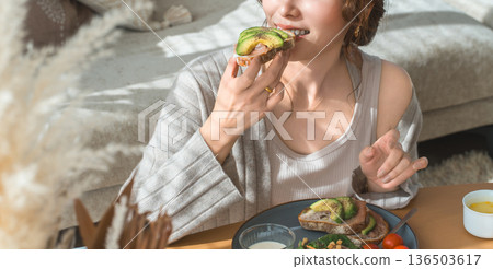 一位時尚的年輕亞裔女性正在客廳餐桌旁用餐。 一位時尚的年輕亞裔女性正在客廳餐桌旁用餐。 136503617