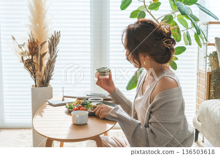 Stylish young Asian woman eating at the living room table Stylish young Asian woman eating at the living room table 136503618