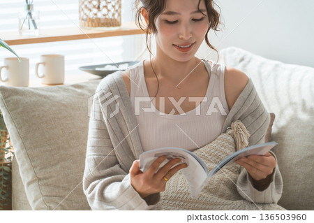 A stylish Asian woman sitting on the sofa in the living room and reading a magazine A stylish Asian woman sitting on the sofa in the living room and reading a magazine 136503960