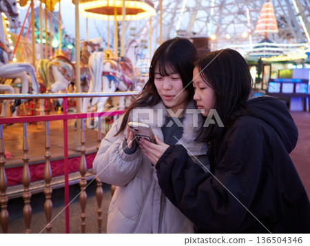 Beautiful illuminations at an amusement park at night and two sisters having fun playing 136504346
