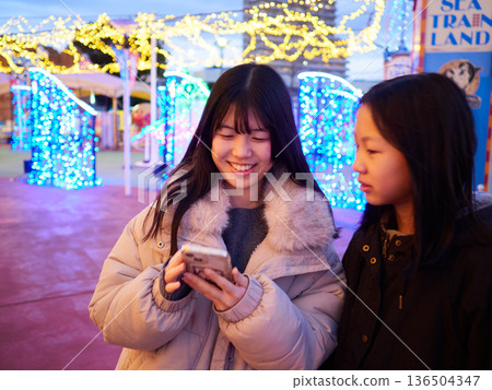 Beautiful illuminations at an amusement park at night and two sisters having fun playing 136504347