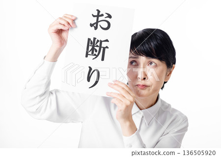 一位身穿白襯衫、表情不悅的老婦人，手裡拿著一張寫著「不」的紙。 136505920