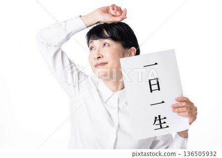 A senior woman smiling and holding a piece of paper with "One day is one life" written on it, raising one hand A senior woman smiling and holding a piece of paper with "One day is one life" written on it, raising one hand 136505932