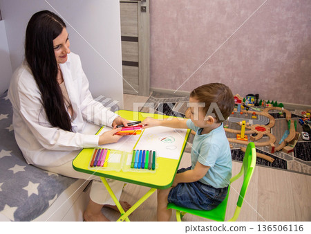 Adult woman and young boy drawing with colorful markers on small green table, learning activity and creative time for child indoors 136506116