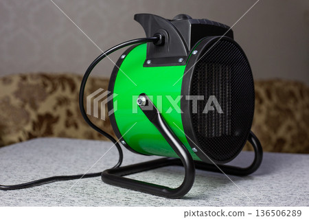 Portable tabletop room heater. Electric heat gun in green cylindrical housing for raising the temperature in cold room. Room heating device. Compact industrial heater Portable tabletop room heater. Electric heat gun in green cylindrical housing for raising the temperature in cold room. Room heating device. Compact industrial heater 136506289