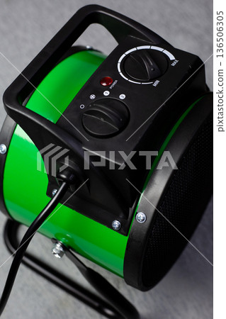 Close-up photo of electric air heater. Green heater with a cord. Plugging the appliance into a power outlet. Insulated cord from powerful home heater, vertical photo 136506305