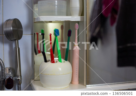 Toothbrushes of various colors stand in holder on bathroom shelf. Scene includes mirror reflecting towels. Authentic bathroom is clean and organized Toothbrushes of various colors stand in holder on bathroom shelf. Scene includes mirror reflecting towels. Authentic bathroom is clean and organized 136506501