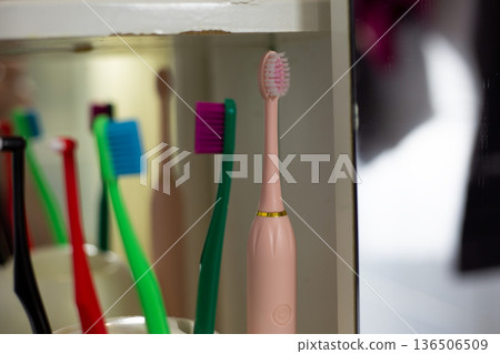 Electric toothbrush on shelf next to regular plastic toothbrushes. Upgrading to new electric toothbrush. Technology for daily routine. Device for cleaning teeth using vibrations. Modern oral care Electric toothbrush on shelf next to regular plastic toothbrushes. Upgrading to new electric toothbrush. Technology for daily routine. Device for cleaning teeth using vibrations. Modern oral care 136506509