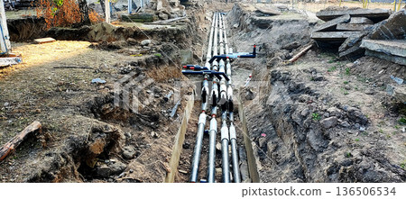 Underground utility pipes installation in trench construction site; infrastructure development project with excavated earth and concrete debris present 136506534