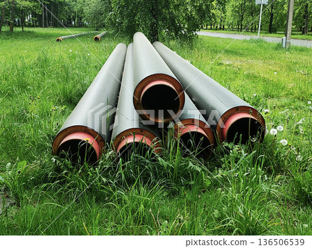 Pipes infrastructure construction material lay on green grass field near road in outdoor day scene with trees and foliage 136506539