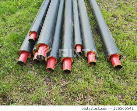 Pre-insulated heating pipes with black outer layer and red inner pipe resting on green grass outdoor storage construction site material 136506541