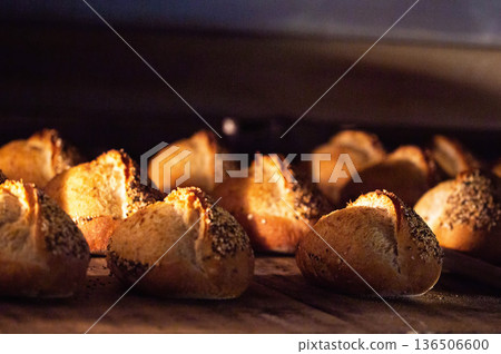 Freshly baked bread rolls with crispy golden crust and seeds, arranged on baking sheet, baking inside warm professional bakery oven 136506600