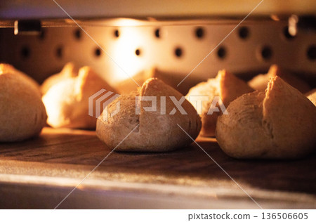 Golden brown bread rolls baking inside industrial oven at bread factory, warm light illuminating crust, traditional bakery product preparation process 136506605