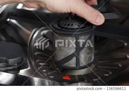 Hand removing dirty filter from dishwasher showing accumulated food residue grime and maintenance process of kitchen appliance 136506611