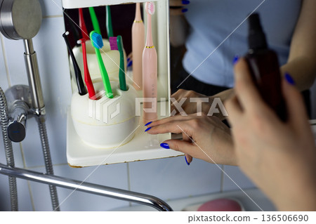Girl opens skincare product in front of mirror in bathroom. Hands remove cap from body spray. Special home care products for health. The process of using skincare products Girl opens skincare product in front of mirror in bathroom. Hands remove cap from body spray. Special home care products for health. The process of using skincare products 136506690