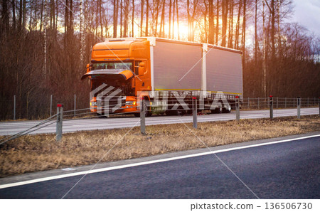 Orange semi-truck with open hood parked on roadside, road transport breakdown, logistics vehicle maintenance, evening sunset 136506730