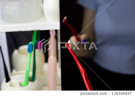 Woman holds single tufted toothbrush in front of bathroom mirror. Single-tufted toothbrush for remove bacterial plaque from gingival sulcus and interdental spaces, ideal for thorough cleaning 136506847