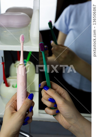 Vertical photo reflecting concept of transition from manual toothbrush to electric toothbrush. Woman holds modern device and conventional one. Modern technologies for cleaning teeth and gums 136506867