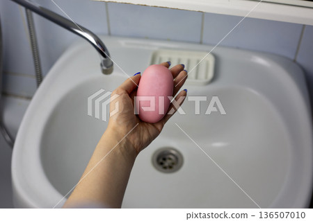 Woman holding soap illustrates concept of handwashing. Natural interior is set against backdrop of hand holding soap. Candid shot demonstrating daily handwashing routine in lived-in bathroom Woman holding soap illustrates concept of handwashing. Natural interior is set against backdrop of hand holding soap. Candid shot demonstrating daily handwashing routine in lived-in bathroom 136507010