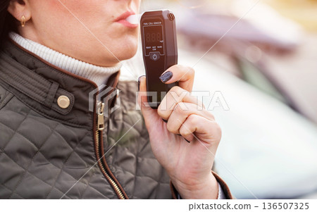Woman Blowing Into Personal Breathalyzer Mouthpiece. Driver Testing For Alcohol Intoxication. Copy space for text Woman Blowing Into Personal Breathalyzer Mouthpiece. Driver Testing For Alcohol Intoxication. Copy space for text 136507325