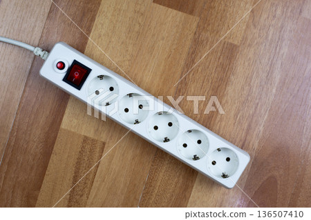 White electrical power strip with a prominent red master switch and safety reset button sits on a rustic wooden floor, emphasizing practical safety in home or workshop environments 136507410