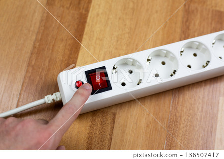 Finger reaches for control on surge protector with power switch and short circuit reset button. Extension cord with protection system during use. Several European two hole charging ports Finger reaches for control on surge protector with power switch and short circuit reset button. Extension cord with protection system during use. Several European two hole charging ports 136507417