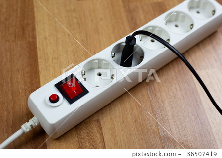 White extension cord with multiple outlets and single red switch and plug from electrical appliance, located on wooden table, demonstrates simplicity and organization in power management White extension cord with multiple outlets and single red switch and plug from electrical appliance, located on wooden table, demonstrates simplicity and organization in power management 136507419