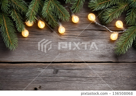 Evergreen branches adorned with warm glowing lights on rustic wooden surface, creating a cozy and inviting atmosphere for festive celebrations and holiday gatherings 136508068