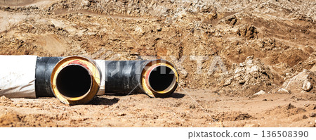 Large black and yellow pipes are placed on the ground at a construction site with dirt and sand around them during the day 136508390