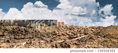 Construction workers are moving dirt at a work site. Clouds build in a blue sky above heavy machinery and fresh earth during the day Construction workers are moving dirt at a work site. Clouds build in a blue sky above heavy machinery and fresh earth during the day 136508393