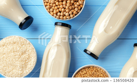 Different types of plant-based milk in glass bottles and bowls on blue background 136508420