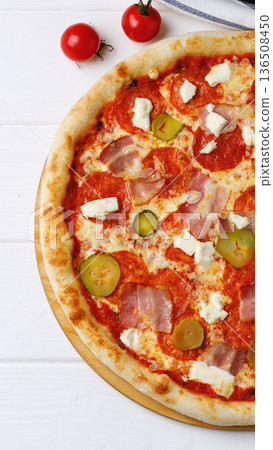 Delicious pizza with toppings on a wooden board next to tomatoes on a table Delicious pizza with toppings on a wooden board next to tomatoes on a table 136508450