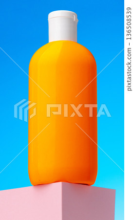 Bright orange bottle stands on a pink platform under a blue sky Bright orange bottle stands on a pink platform under a blue sky 136508539