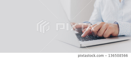 Person types on laptop while sitting at a desk in a bright room during the day Person types on laptop while sitting at a desk in a bright room during the day 136508566