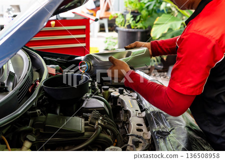 Mechanic pouring engine oil into car engine in garage routine vehicle maintenance service with lubricant bottle and open hood close up detail 136508958