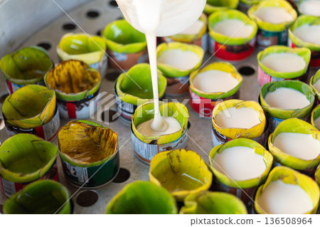 Traditional coconut custard poured into banana leaf cups on metal tray fresh Thai dessert preparation with creamy texture and vibrant green natural presentation Traditional coconut custard poured into banana leaf cups on metal tray fresh Thai dessert preparation with creamy texture and vibrant green natural presentation 136508964