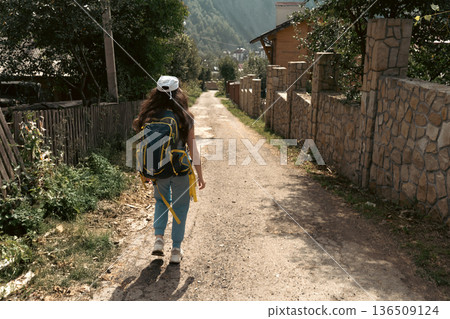 Female Traveler with Backpack Walking Through Mountain Village 136509124