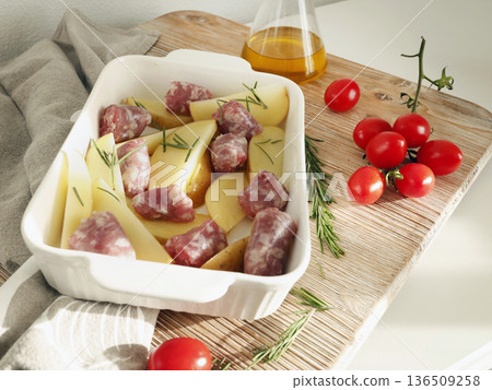 Potato wedges and homemade sausages made from farm-raised meat, prepared for baking in ceramic dish. Food and health. Spices and natural products. 136509258