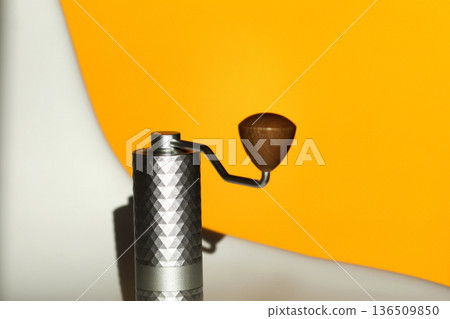Manual Coffee Grinder Close-up. A close-up shot of the top part of a modern manual coffee grinder with a textured metallic grey body and a wooden handle knob 136509850