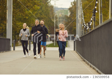 Group of runners jogging together on city bridge in park during fitness training 136509958