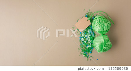 Recycled plastic pellets and skeins of green polyester thread with blank paper tag symbolizing circular sustainability, eco-friendly manufacturing Recycled plastic pellets and skeins of green polyester thread with blank paper tag symbolizing circular sustainability, eco-friendly manufacturing 136509986