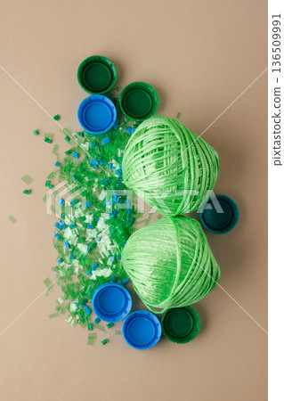 Plastic bottle caps, shredded plastic, and balls of polyester yarn symbolize recycling process and the concept of circular economy and green technologies Plastic bottle caps, shredded plastic, and balls of polyester yarn symbolize recycling process and the concept of circular economy and green technologies 136509991