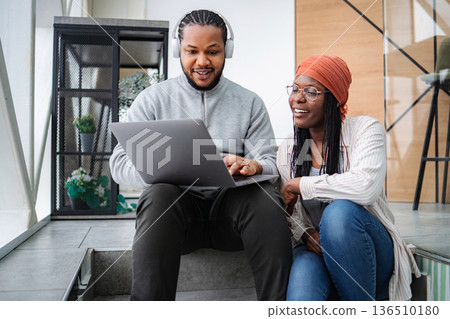 Young adult couple collaborating on laptop wearing headphones and smiling 136510180