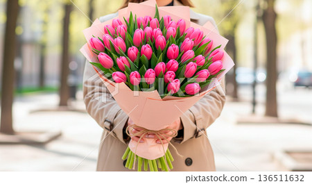 Woman holding a large bouquet of vibrant pink tulips wrapped in delicate pink paper 136511632