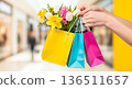 Hands holding colorful shopping bags filled with fresh spring flowers in a mall 136511657