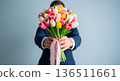 Man in a suit offers a vibrant bouquet of colorful tulips tied with a pink ribbon 136511661