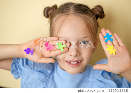 Stickers in the shape of puzzles and hearts decorate the face and palm of a beautiful girl. World Autism Awareness Day. A symbol of education, reason, and people with autism spectrum disorders Stickers in the shape of puzzles and hearts decorate the face and palm of a beautiful girl. World Autism Awareness Day. A symbol of education, reason, and people with autism spectrum disorders 136511818