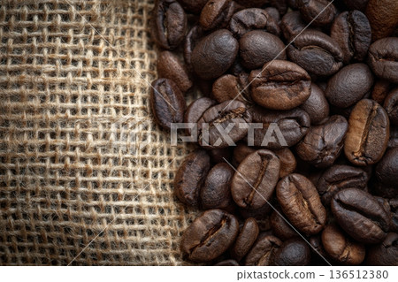 Dark coffee beans glisten with rich oils, set against a rustic burlap background, evoking warmth and the art of brewing 136512380